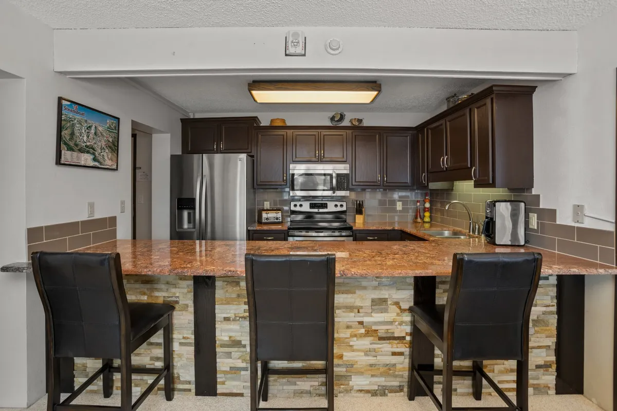 Displaying a sleek, modern kitchen with granite countertops, dark wooden cabinets, and stainless steel appliances, this image highlights the space’s functionality and style. The work surfaces and appliances are the clear focus, emphasizing the kitchen's readiness for any cooking adventure.