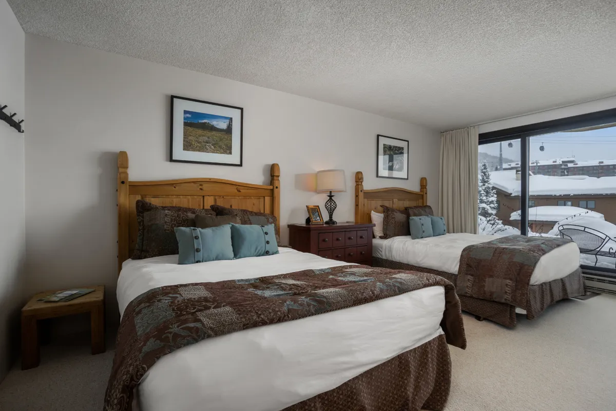 A cozy bedroom with wooden bed frames, decorative pillows, and large windows revealing a snowy, tranquil landscape. Soft lighting and tasteful artwork add to the comfortable, home-like atmosphere, inviting guests to unwind after a day of adventure.