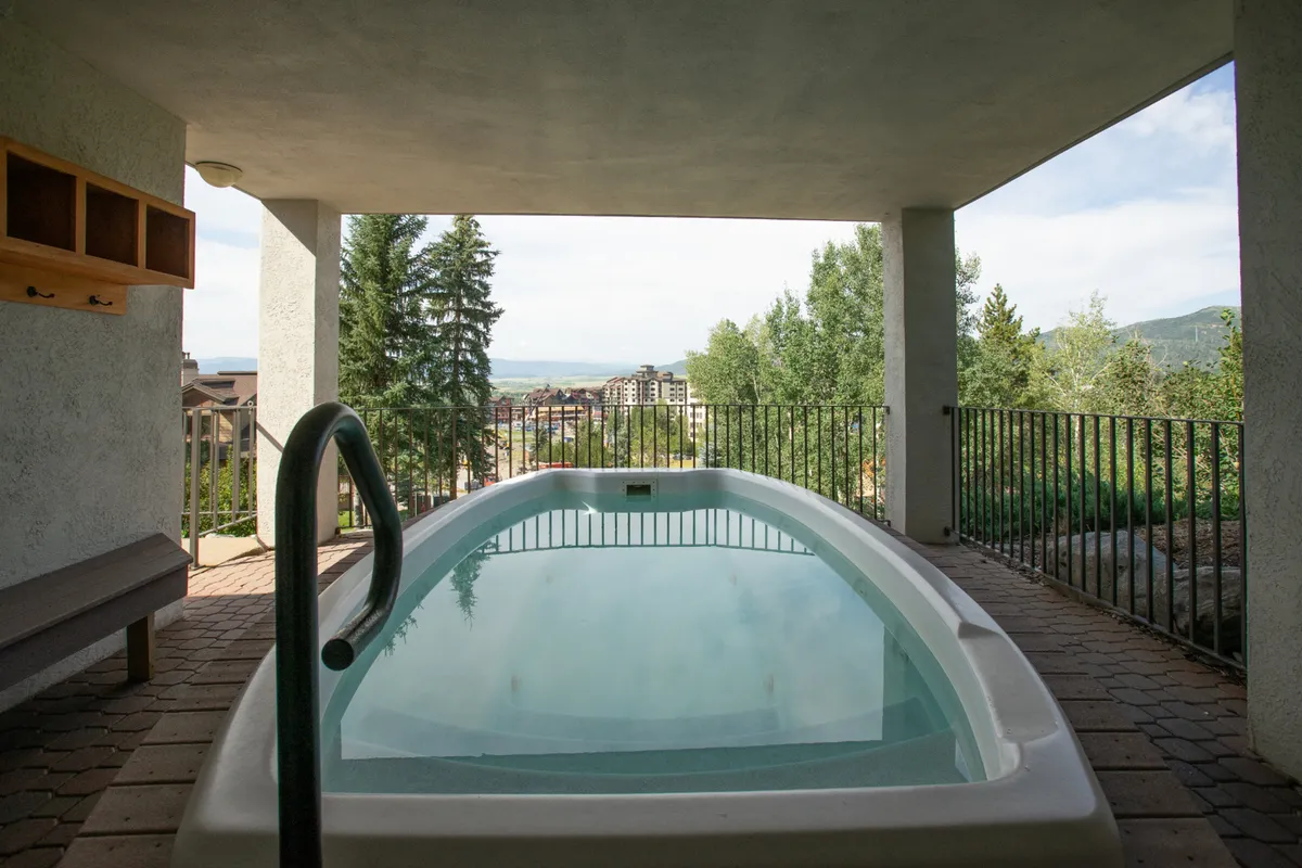 An exterior hot tub area with a stunning mountain view, wooden bench, and railings. People can be seen relaxing in the hot tub, enjoying the tranquil setting and panoramic vistas, ideal for both kids and adults.