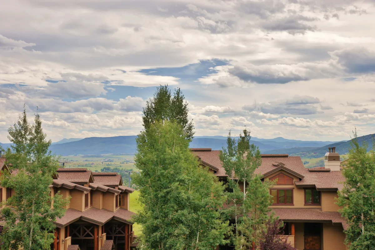 A tranquil exterior view featuring lush green trees, a sweeping mountain range under a cloudy sky, and glimpses of the property's architectural details. The scene suggests peaceful outdoor activities such as hiking and nature walks, with opportunities for sunset viewing and stargazing.
