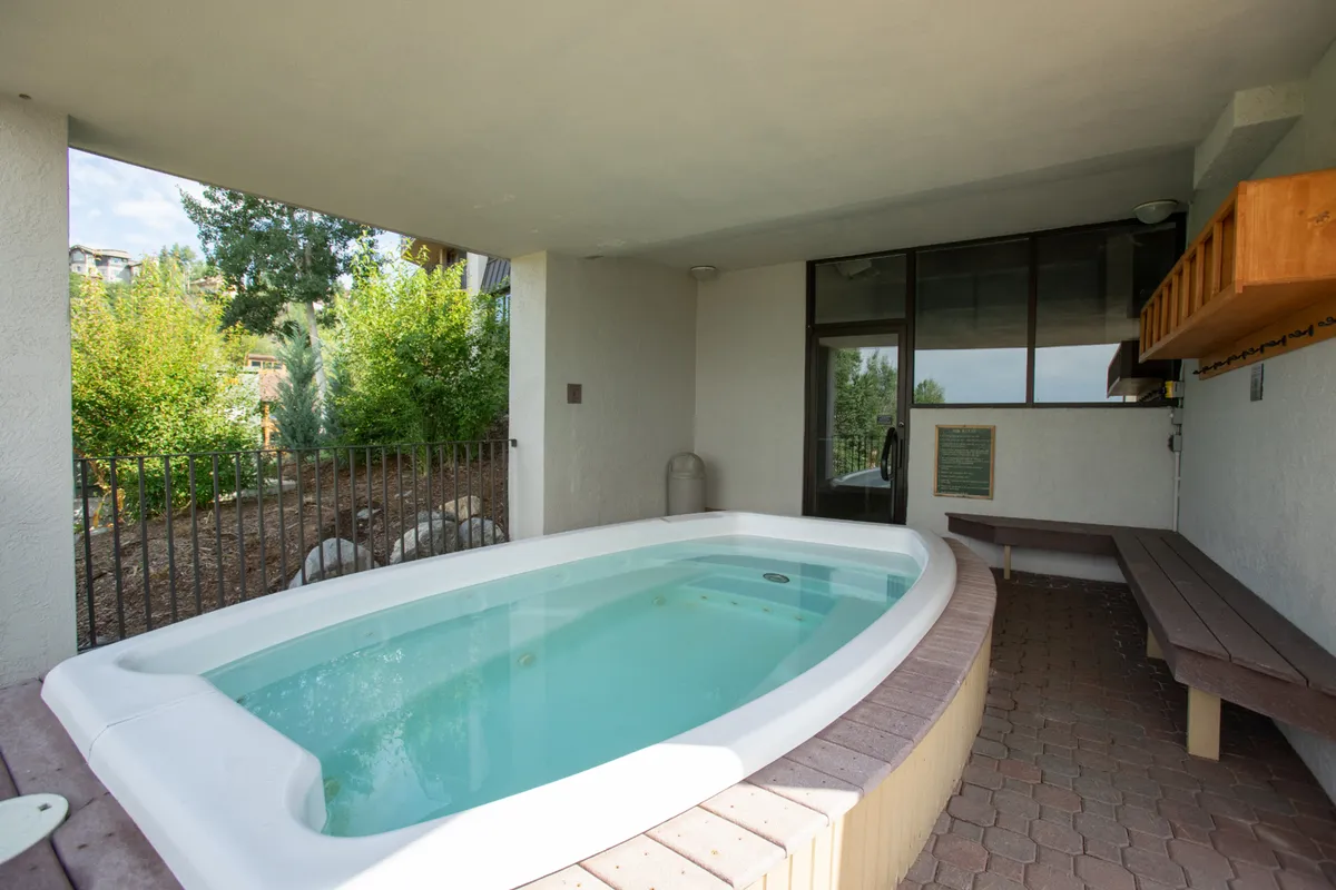 An inviting indoor hot tub area with benches and large windows framing nature outside. The space is tranquil, perfect for relaxation and soaking while gazing out at the surrounding environment.