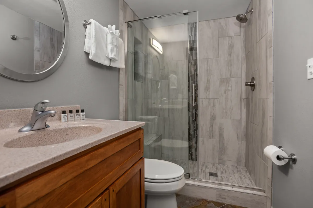 A stylish bathroom featuring a vanity with a solid-surface counter, a modern sink, a glass shower enclosure, and a toilet. The space feels fresh and tranquil, ideal for self-care routines and relaxation after a long day.