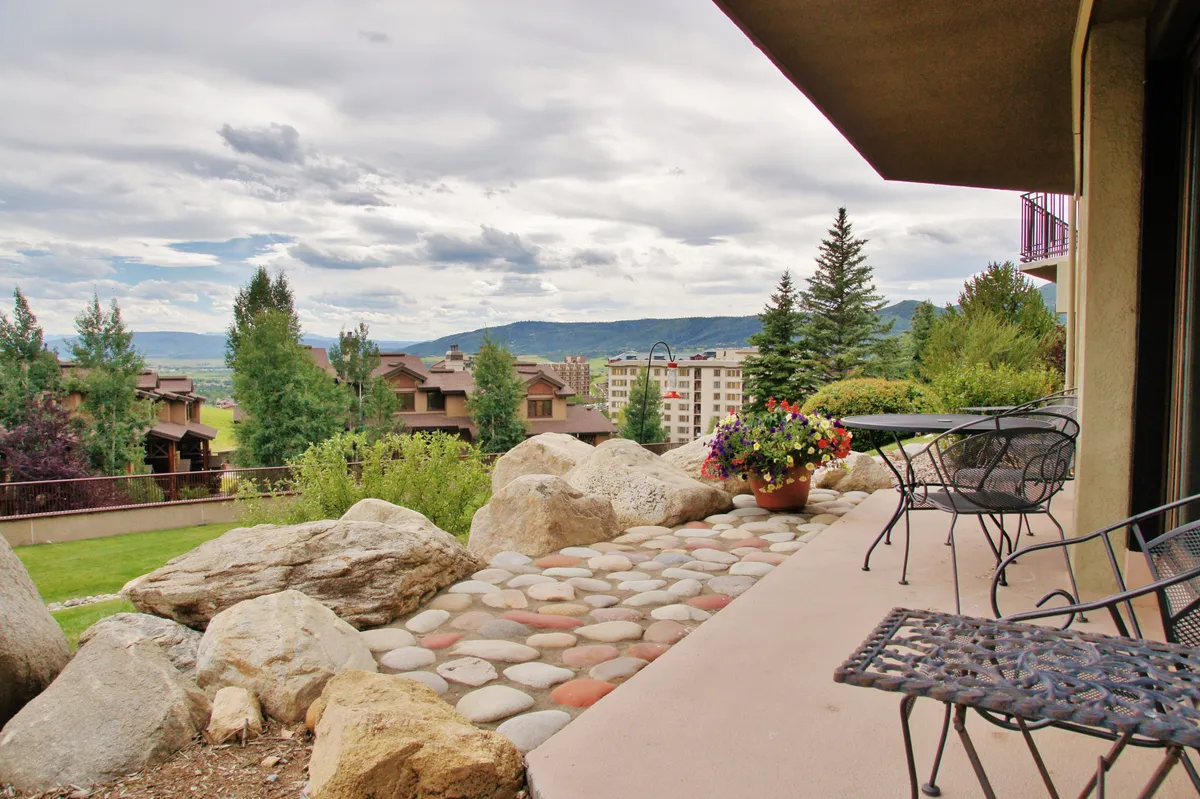 A serene exterior patio space with comfortable furniture and a flower pot, set against a backdrop of dramatic rock formations and panoramic mountain views. The area exudes calm, making it an ideal spot for relaxation or enjoying the beauty of nature.