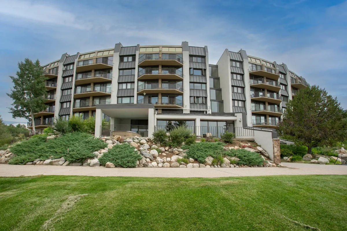 A contemporary building with modern architecture surrounded by lush, landscaped greenery. Spacious balconies overlook the gardens, where people are seen relaxing and socializing in the outdoor area. The setting exudes a welcoming and family-friendly atmosphere.
