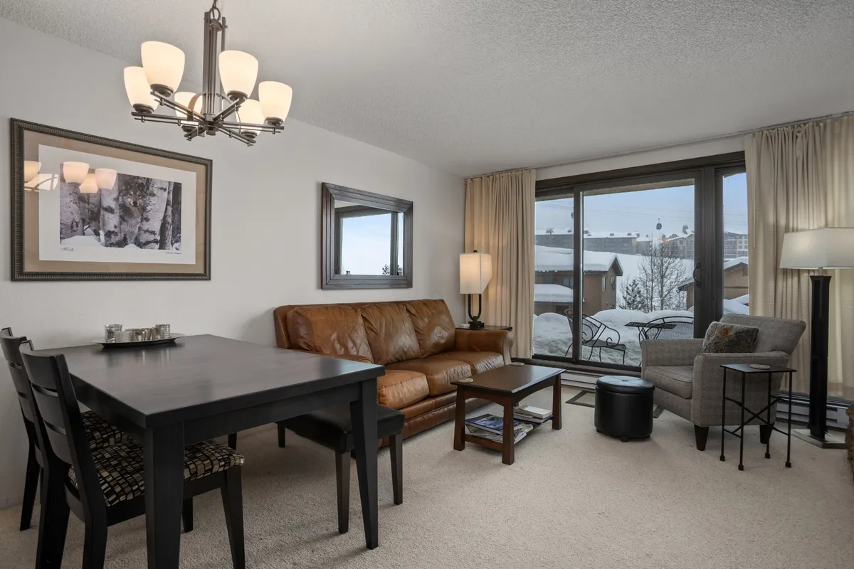 An open-plan living and dining area furnished with a leather sofa and a large dining table. Floor-to-ceiling windows provide stunning views, filling the space with natural light. The area feels inviting and sets the scene for both casual breakfasts and lively evening gatherings.